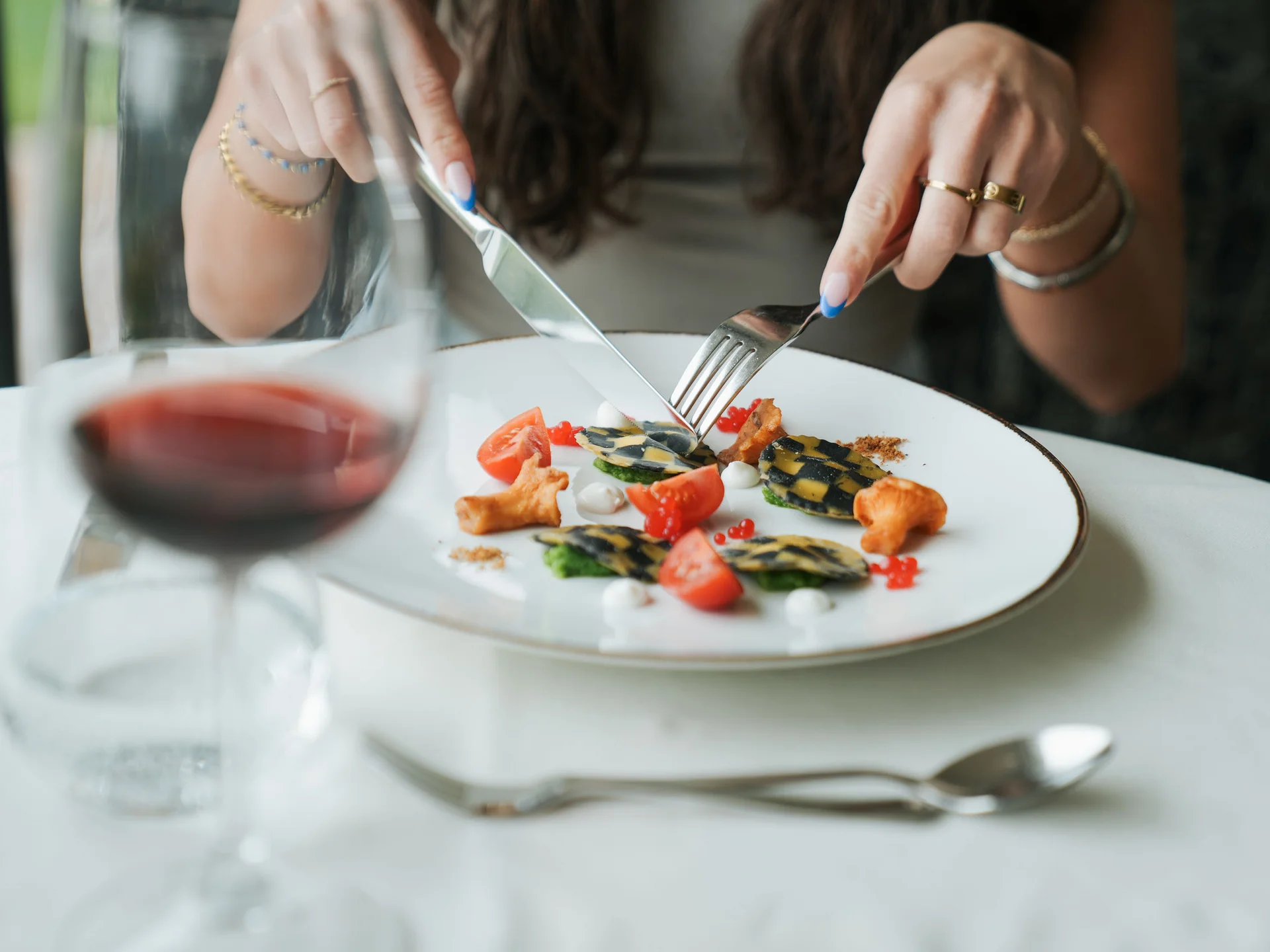Euer Hotel in Schenna für Momente in #echtzeit Person schneidet Gourmetgericht auf weißem Teller mit Rotwein im Vordergrund