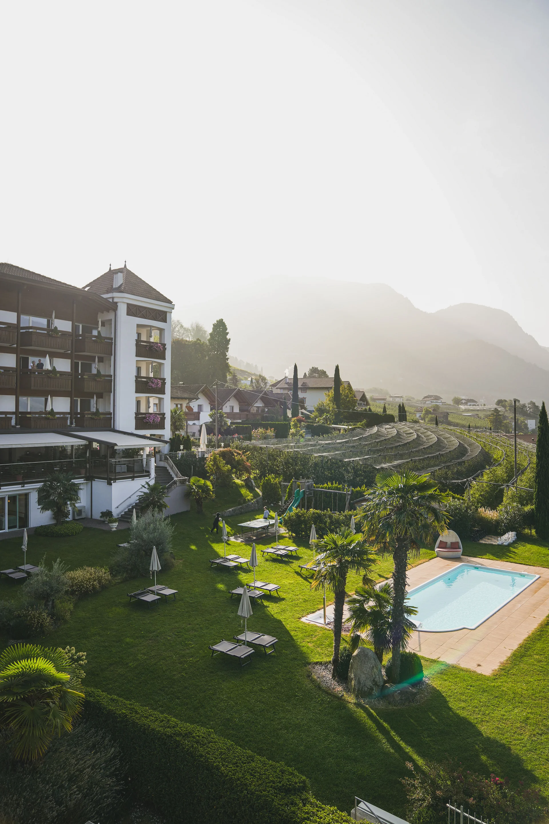 Euer Hotel in Schenna für Momente in #echtzeit Hotel mit Garten, Pool und Weinbergen in sonniger Landschaft mit Bergen im Hintergrund