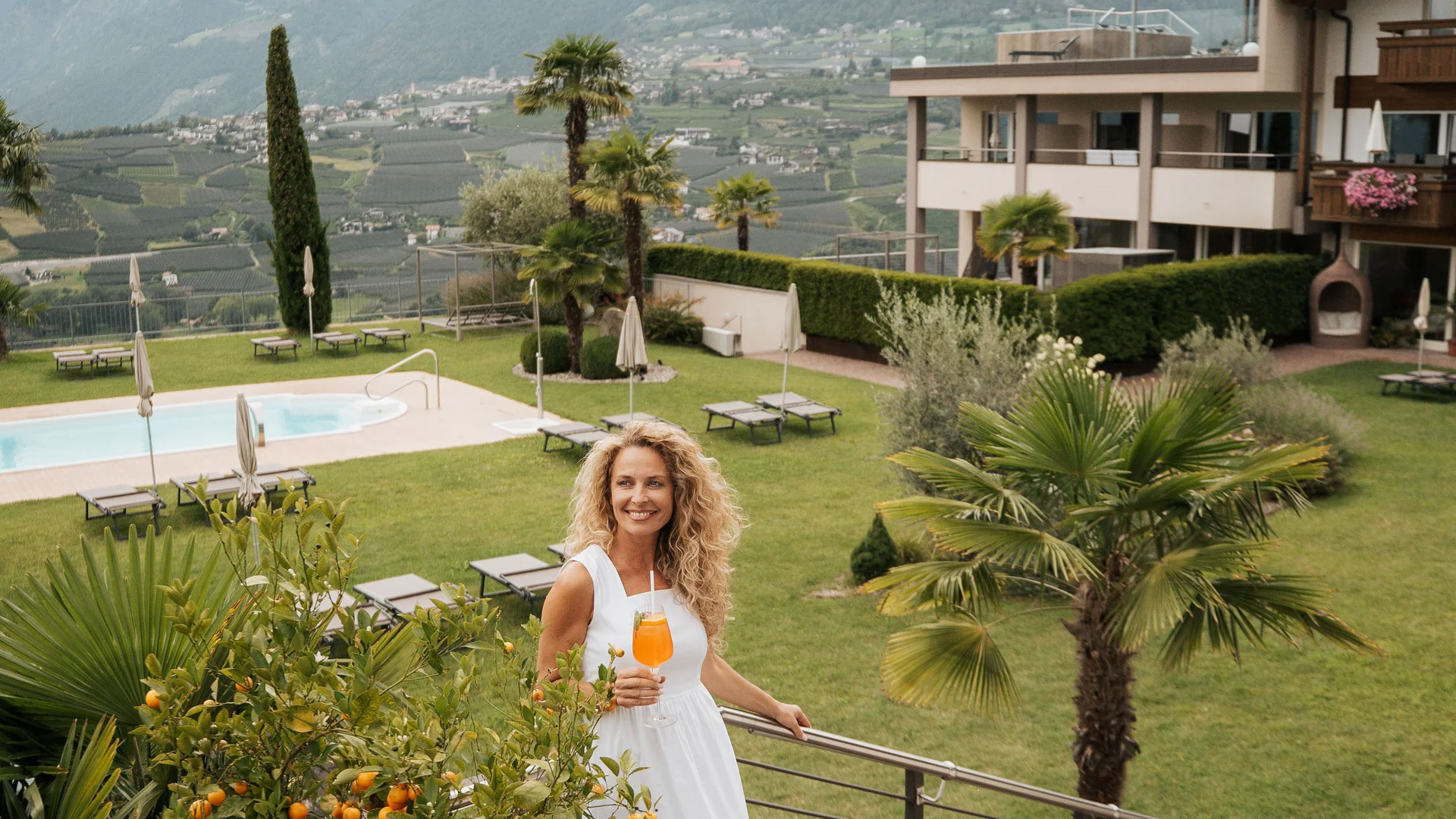 Euer Hotel in Schenna für Momente in #echtzeit Frau in weißem Kleid mit Getränk auf Treppe mit Bergblick im Hintergrund