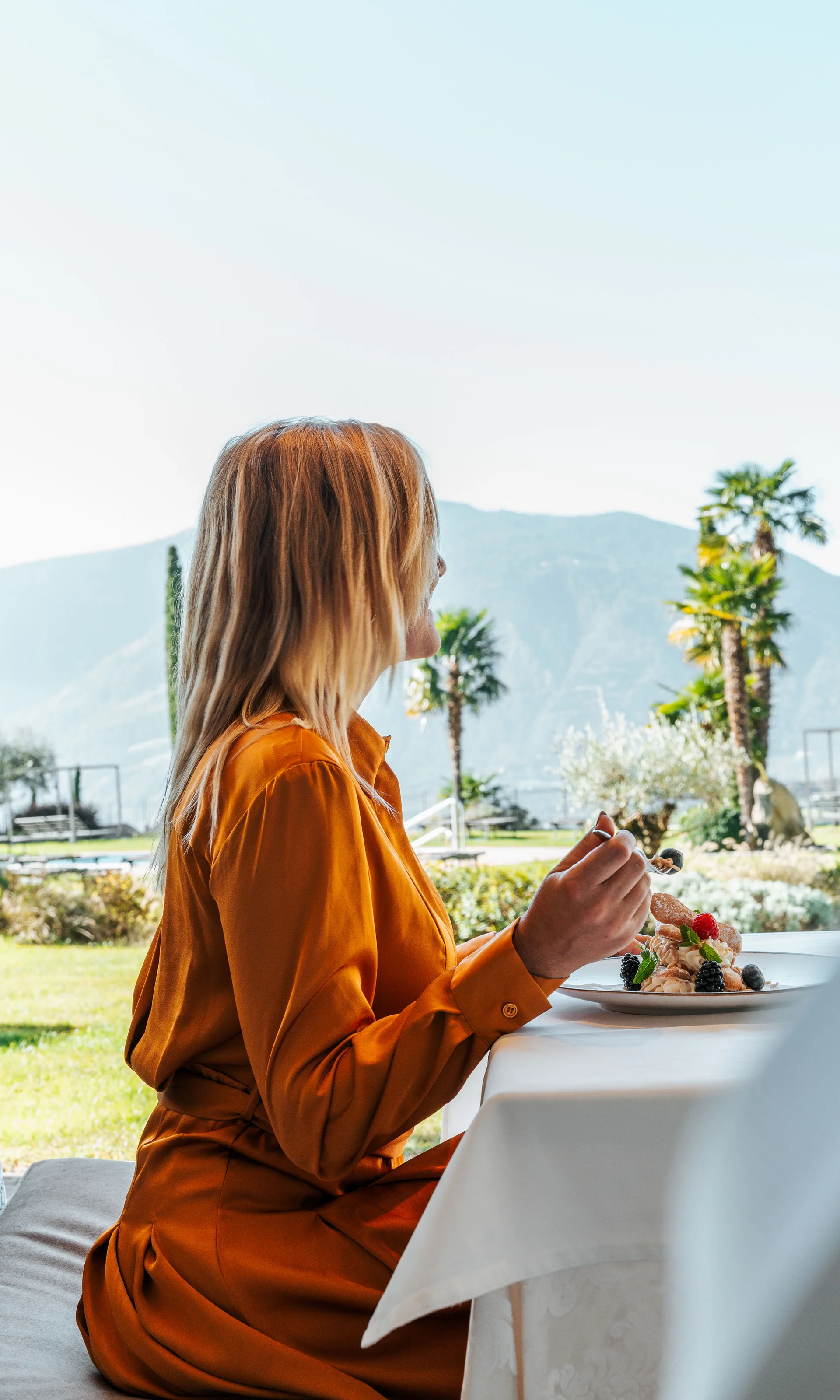 Euer Hotel in Schenna für Momente in #echtzeit Frau in orangefarbener Kleidung isst im Freien mit Bergblick