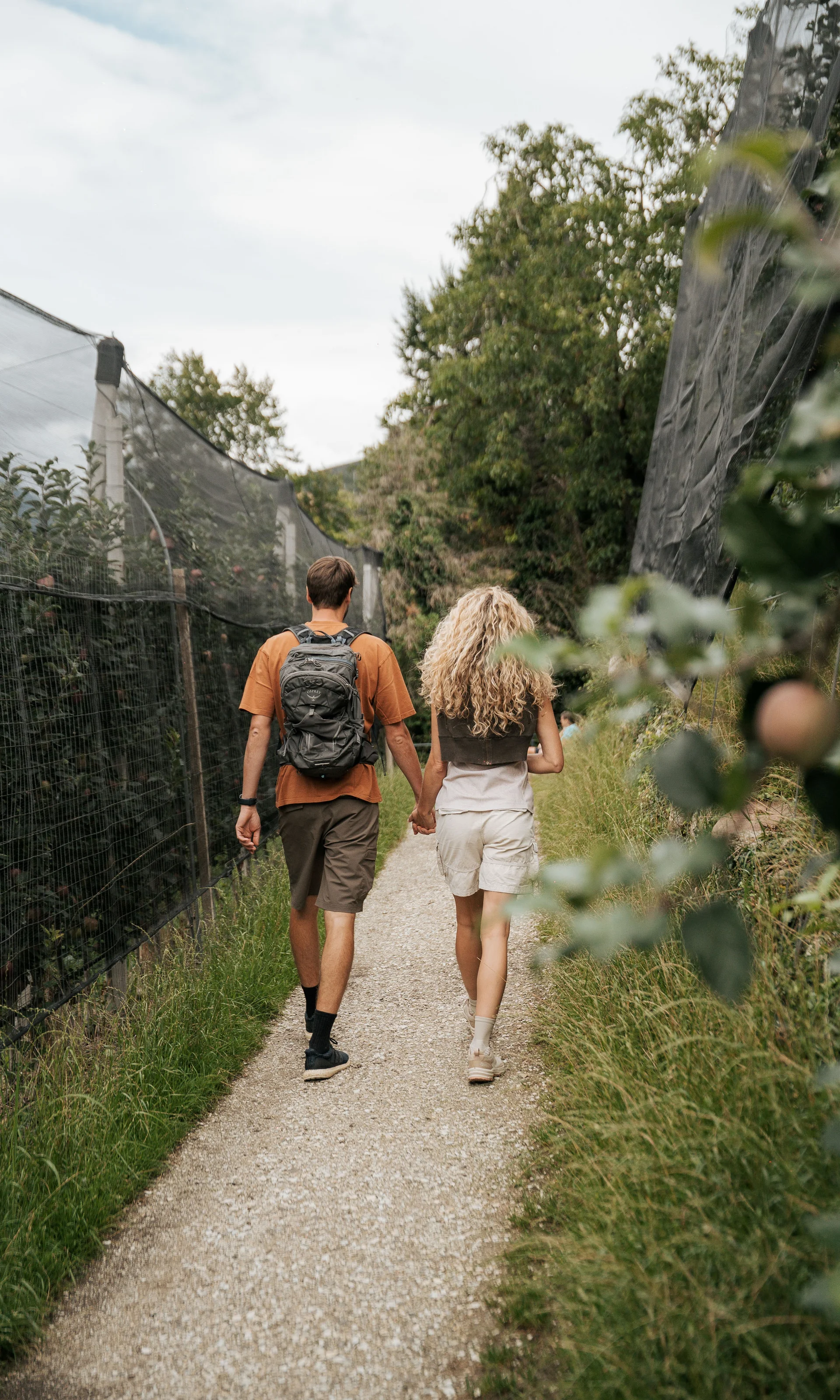 Euer Hotel in Schenna für Momente in #echtzeit Paar spaziert Hand in Hand auf einem Weg zwischen Bäumen und Netzen